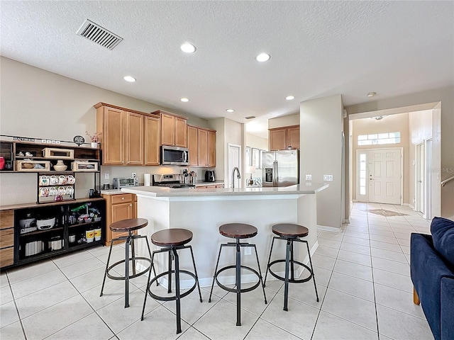 kitchen with light tile patterned floors, appliances with stainless steel finishes, a breakfast bar area, a textured ceiling, and a kitchen island with sink