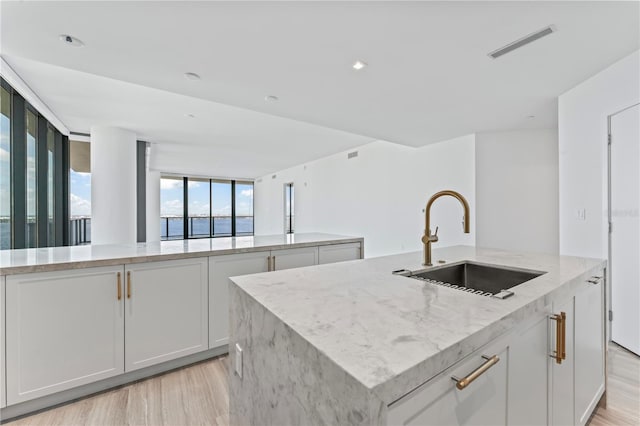 kitchen featuring white cabinetry, light stone counters, light hardwood / wood-style floors, and a kitchen island with sink