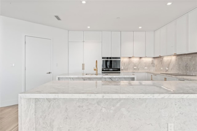 kitchen featuring light hardwood / wood-style floors, white cabinets, decorative backsplash, black appliances, and light stone countertops