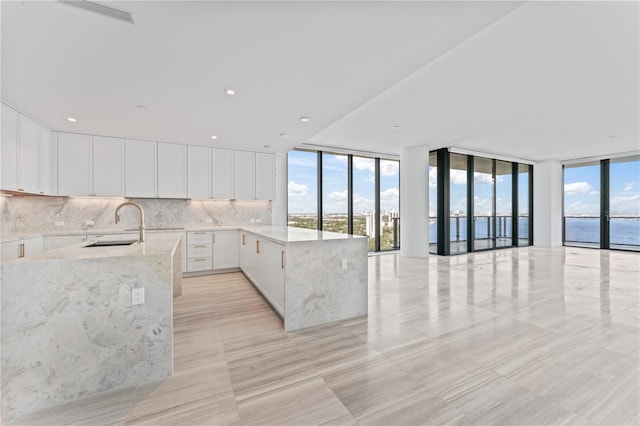 kitchen with light stone counters, white cabinetry, expansive windows, decorative backsplash, and a water view