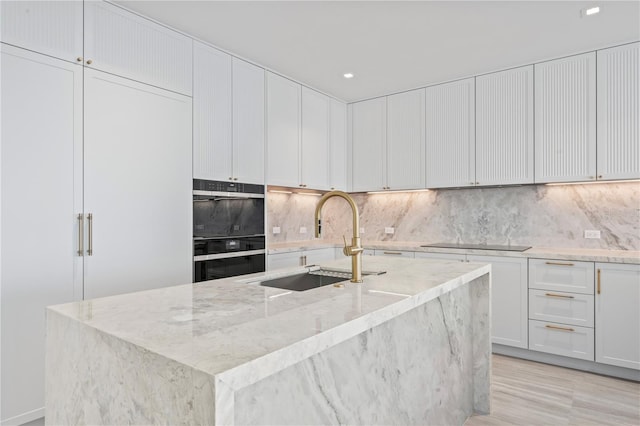 kitchen with white cabinetry, sink, black appliances, light stone countertops, and a kitchen island with sink