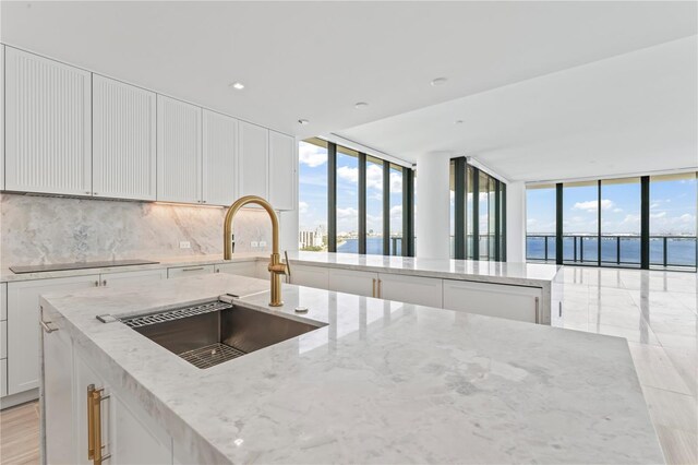 kitchen with a water view, a center island with sink, sink, tasteful backsplash, and light stone countertops