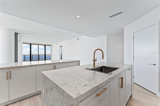 kitchen with a water view, white cabinets, sink, a kitchen island with sink, and light wood-type flooring