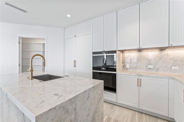 kitchen with sink, light stone counters, an island with sink, white cabinets, and decorative backsplash