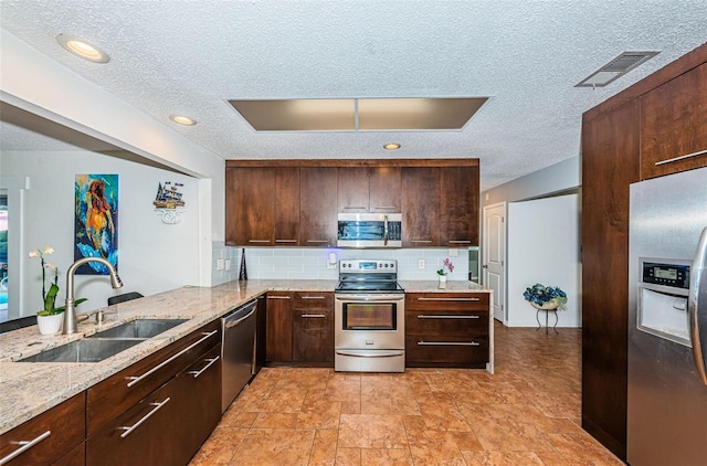 kitchen featuring stainless steel appliances, decorative backsplash, kitchen peninsula, sink, and light stone countertops