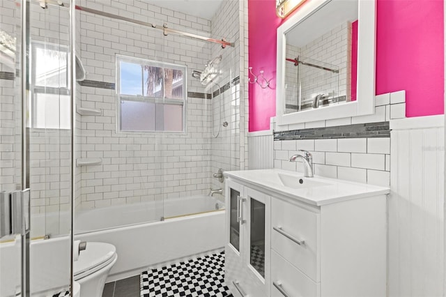 full bathroom with toilet, bath / shower combo with glass door, vanity, and tile walls