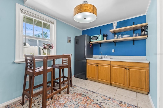 kitchen with light tile patterned floors, crown molding, sink, and black fridge