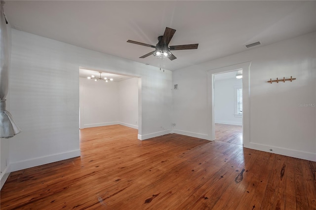 empty room with hardwood / wood-style floors and ceiling fan with notable chandelier