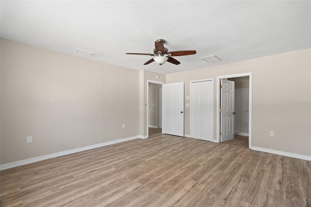 unfurnished bedroom featuring a textured ceiling, light wood-type flooring, ensuite bathroom, and ceiling fan