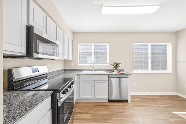 kitchen with appliances with stainless steel finishes, light hardwood / wood-style floors, white cabinetry, and sink