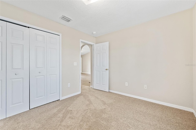 unfurnished bedroom featuring light carpet, a textured ceiling, and a closet