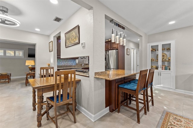 kitchen with tasteful backsplash, sink, kitchen peninsula, a kitchen breakfast bar, and stainless steel fridge