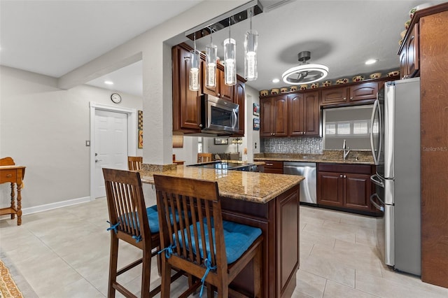 kitchen featuring kitchen peninsula, stainless steel appliances, a breakfast bar, light stone countertops, and pendant lighting