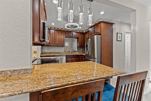 kitchen featuring kitchen peninsula, tasteful backsplash, hanging light fixtures, a breakfast bar area, and appliances with stainless steel finishes