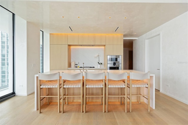 kitchen featuring kitchen peninsula, light brown cabinetry, light wood-type flooring, and stainless steel double oven