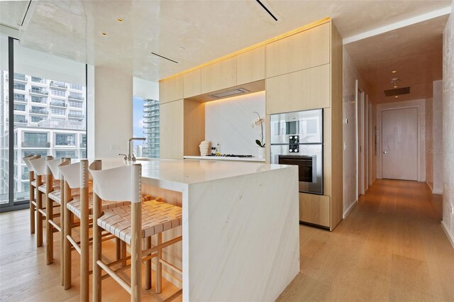 kitchen with light brown cabinetry, a kitchen bar, a center island, stainless steel double oven, and light hardwood / wood-style flooring