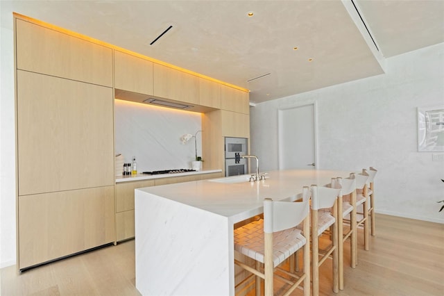 kitchen featuring light brown cabinetry, light wood-type flooring, and an island with sink