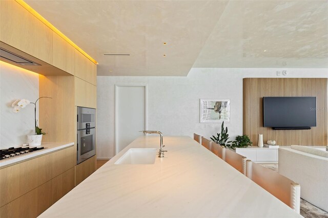 kitchen with light brown cabinetry, sink, double oven, and white gas cooktop