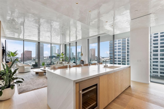 kitchen featuring wine cooler, a wall of windows, an island with sink, and light hardwood / wood-style floors