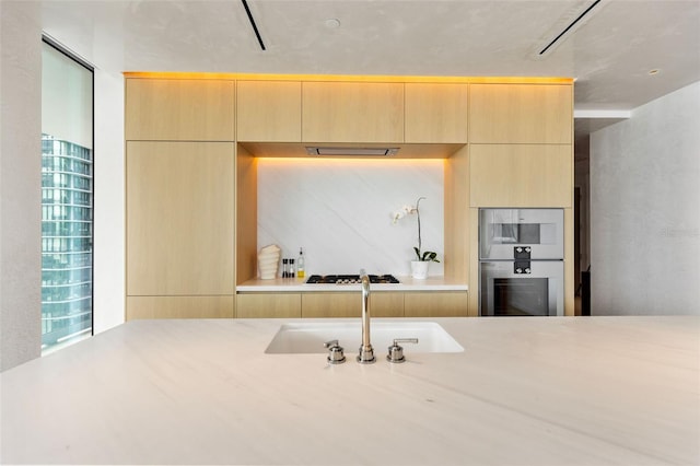 kitchen featuring white gas stovetop, light brown cabinets, double oven, and sink