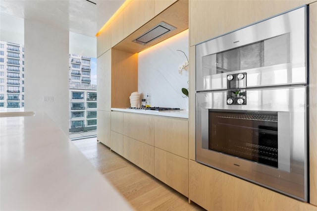 kitchen featuring light hardwood / wood-style floors, light brown cabinetry, white gas stovetop, and stainless steel double oven