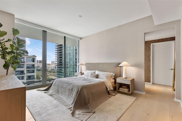 bedroom featuring floor to ceiling windows, light hardwood / wood-style floors, and access to outside