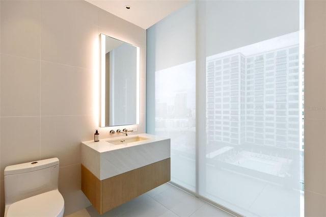 bathroom featuring toilet, vanity, tile patterned floors, and tile walls