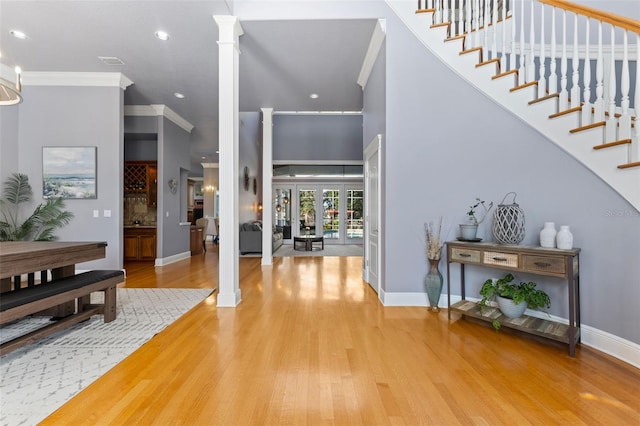 foyer with french doors, wood-type flooring, ornate columns, and crown molding