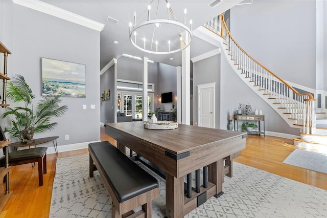 dining space with a high ceiling, a chandelier, ornamental molding, and light hardwood / wood-style flooring