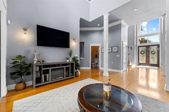 living room featuring a high ceiling, ornate columns, light hardwood / wood-style flooring, and crown molding