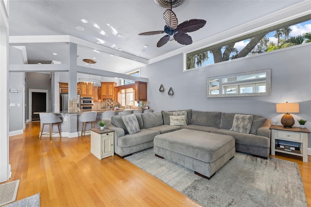 living room with ceiling fan, light wood-type flooring, high vaulted ceiling, and ornamental molding