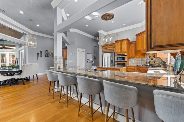 kitchen featuring stainless steel appliances, dark stone countertops, decorative light fixtures, and light wood-type flooring