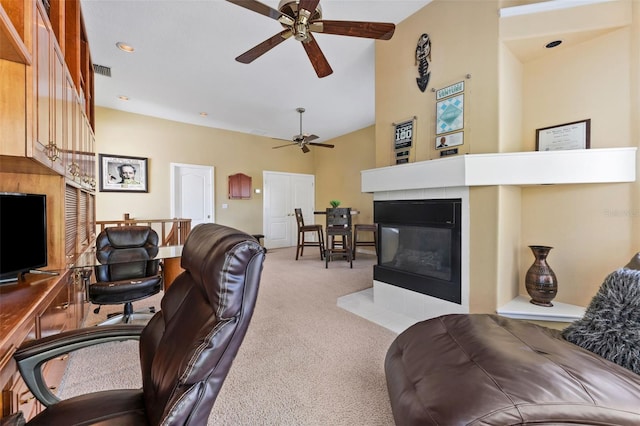 living room with a towering ceiling, a tiled fireplace, light carpet, and ceiling fan