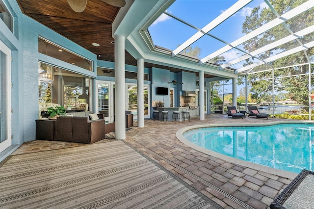 view of pool with glass enclosure, exterior bar, a patio, outdoor lounge area, and ceiling fan