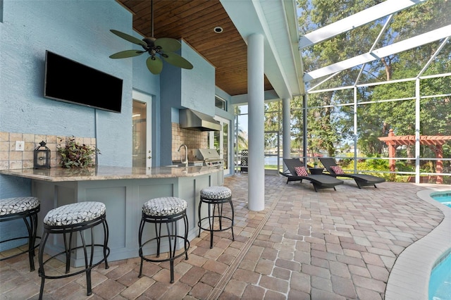 view of patio with glass enclosure, an outdoor wet bar, exterior kitchen, area for grilling, and ceiling fan