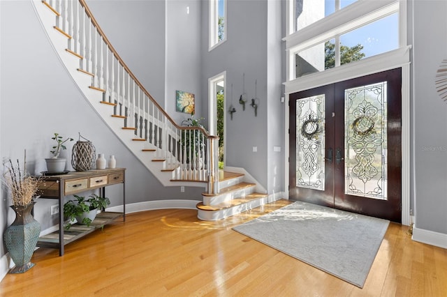 foyer entrance with a towering ceiling, wood-type flooring, and french doors