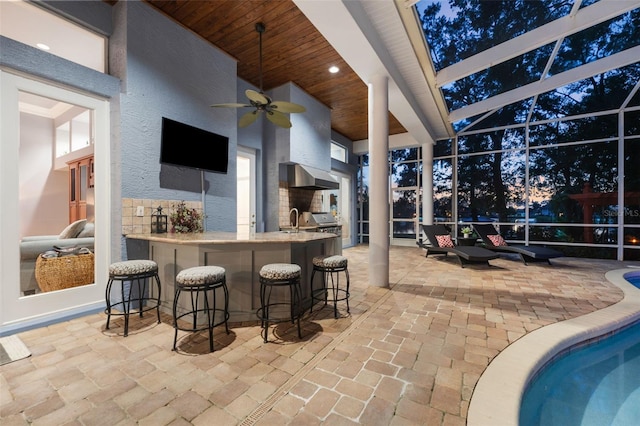 view of patio / terrace featuring a wet bar, glass enclosure, exterior kitchen, and ceiling fan