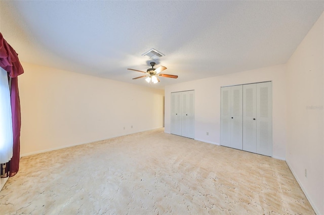 unfurnished bedroom with two closets, a textured ceiling, and ceiling fan