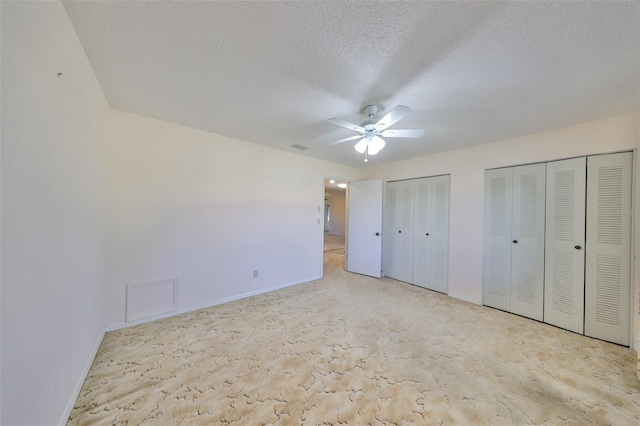 unfurnished bedroom with light carpet, a textured ceiling, multiple closets, and ceiling fan