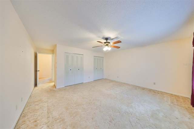 unfurnished bedroom featuring a textured ceiling, two closets, and ceiling fan