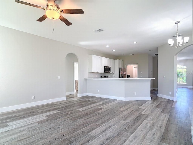 unfurnished living room featuring sink, ceiling fan with notable chandelier, and light wood-type flooring