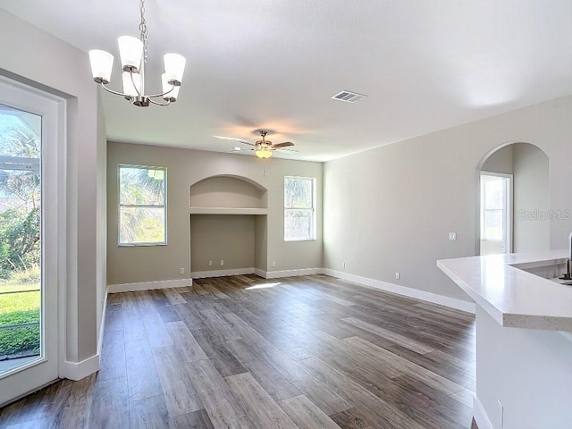 unfurnished living room featuring built in features, wood-type flooring, and ceiling fan with notable chandelier