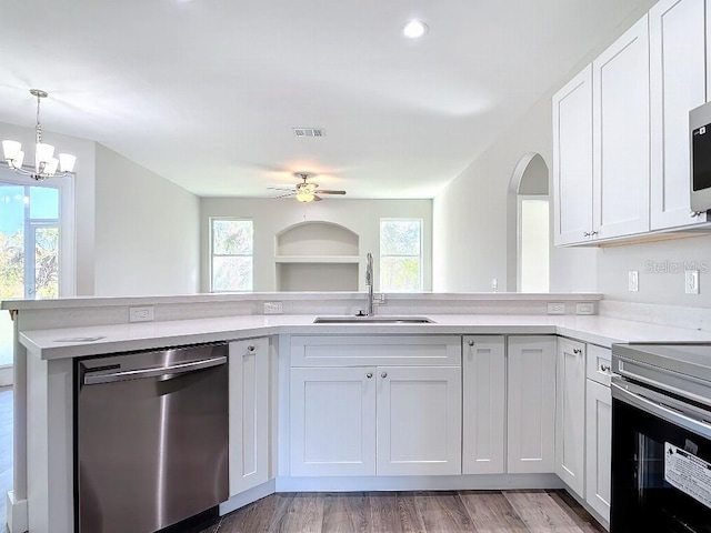 kitchen with sink, kitchen peninsula, white cabinetry, stainless steel appliances, and decorative light fixtures