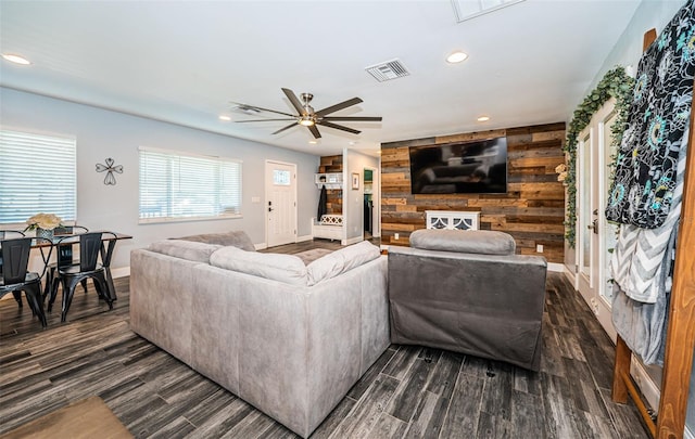 living room with ceiling fan, wood walls, and dark hardwood / wood-style flooring