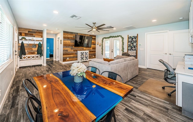 dining space with ceiling fan, a healthy amount of sunlight, dark hardwood / wood-style flooring, and wood walls