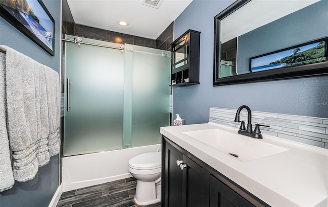 full bathroom with wood-type flooring, combined bath / shower with glass door, toilet, vanity, and decorative backsplash