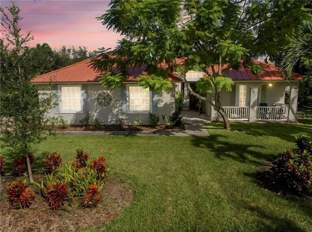 view of front of property with stucco siding, a porch, metal roof, and a front yard