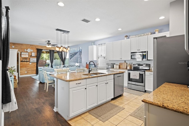 kitchen featuring an island with sink, stainless steel appliances, sink, decorative light fixtures, and white cabinetry