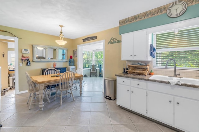 kitchen featuring hanging light fixtures, sink, white cabinets, light tile patterned floors, and dark stone countertops