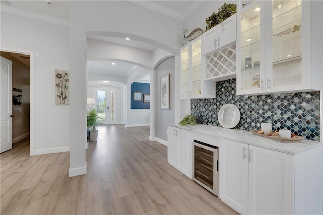 bar featuring wine cooler, light wood-type flooring, ornamental molding, light stone countertops, and white cabinets